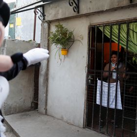 En agosto de 2016, durante la cuarentena en Argentina, un voluntario disfrazado como Mickey Mouse saluda a una niña encerrada en casa en Fuerte Apache, Buenos Aires. Fue una campaña por el Día del Niño en el país para animar a los más pequeños.
