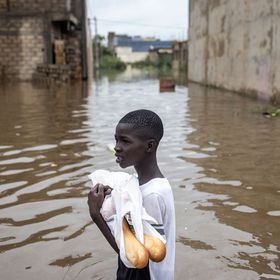 A young boy carries baguettes through the flooded neighbourhood of Keur Massar, Dakar, on August 20, 2021. - Each year the neighbourhood of Keur Massar deals with heavy flooding during the peak of the rainy season. Families living in Keur Massar pack up their belongings and move out of the area during this period. Last year, after the worst flooding to date, the government gave over fifteen million West African Francs towards a project to help fight the flooding and displacement in this area. (Photo by JOHN WESSELS / AFP)