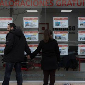 Dos jóvenes miran un escaparate con anuncios de pisos en el Ensanche de Vallecas (Madrid).