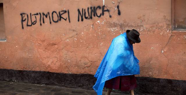 Una mujer indígena camina junto a un graffiti en contra de Fujimori.