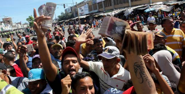 Venezolanos muestran billetes de 100 bol&iacute;vares.