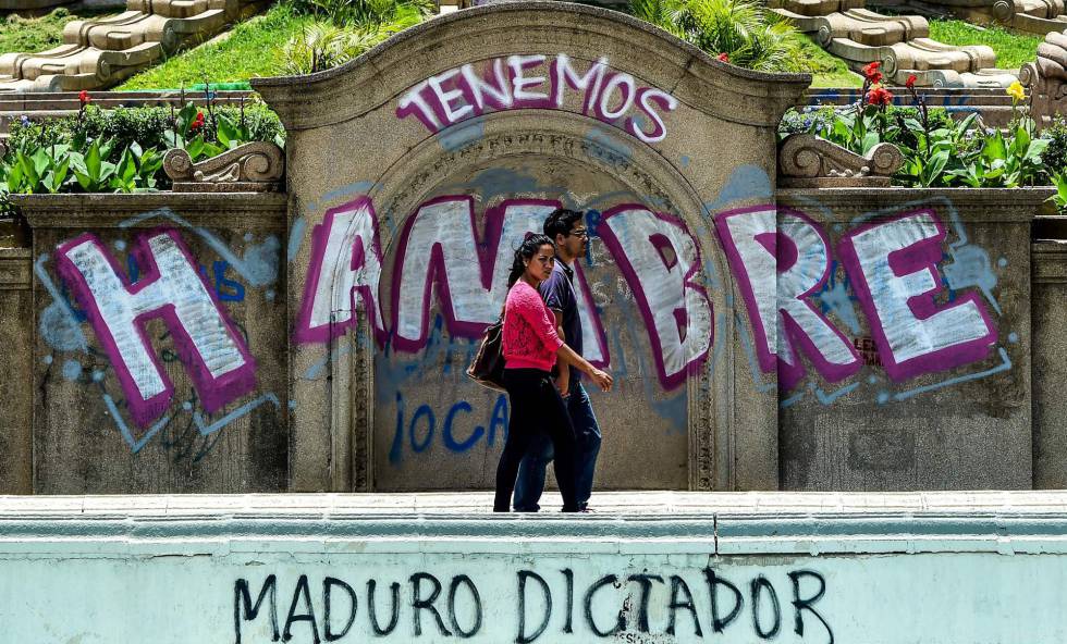 Una pareja pasea frente a un grafiti de protesta contra el Gobierno venezolano.