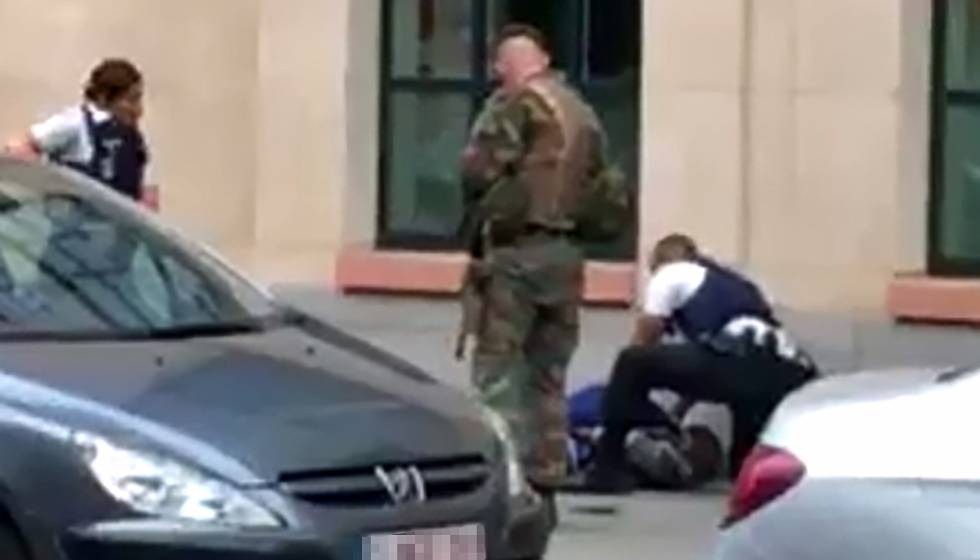 Policías y un soldado rodean a un hombre tendido en el suelo en el lugar donde dos soldados han sido atacados en el centro de Bruselas. 