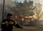 A firefighter reacts as a house burns during a wildfire in Kineta, near Athens, on July 23, 2018.  More than 300 firefighters, five aircraft and two helicopters have been mobilised to tackle the