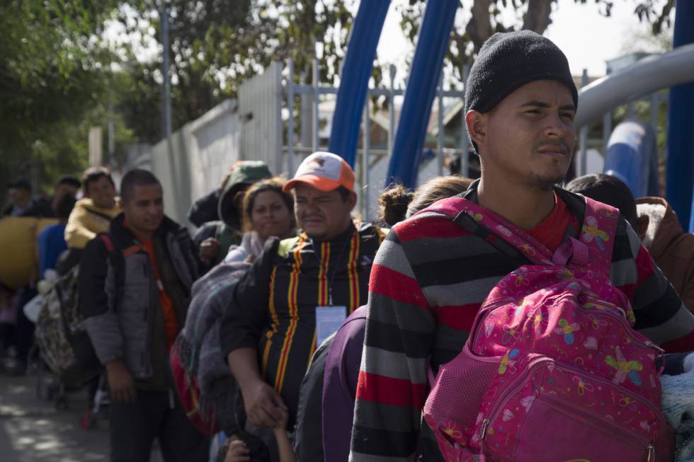Integrantes de la caravana migrante esperan en fila para entrar al albergue temporal en Tijuana.