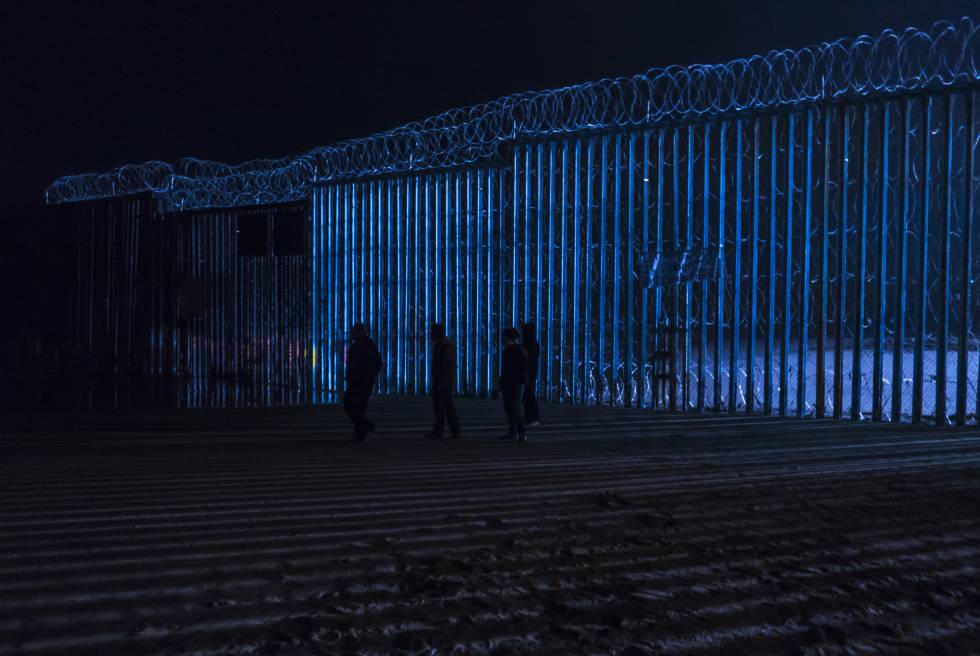 Un grupo de personas camina frente al muro fronterizo de Tijuana, el pasado viernes por la noche.