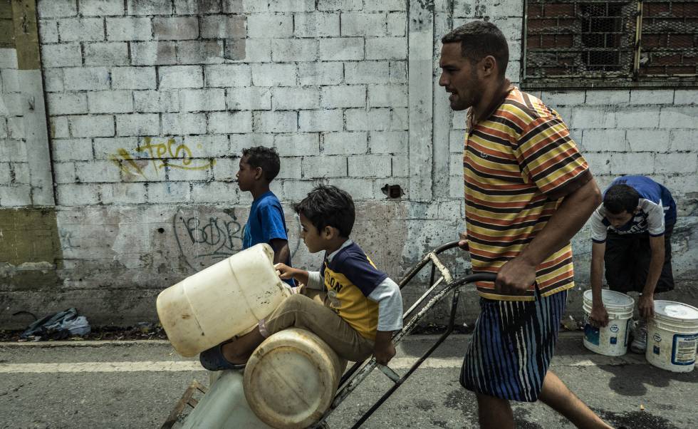 Un hombre y sus hijos portan garrafas de agua en Caracas.