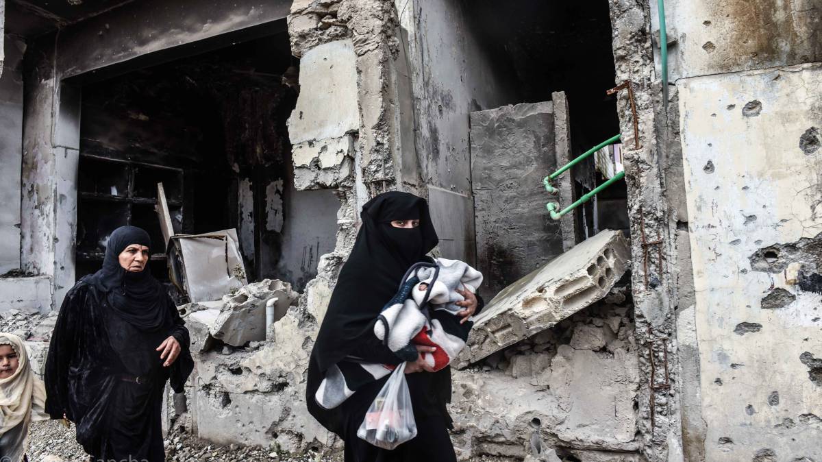 Dos mujeres caminan con sus hijos frente a un edificio en ruinas en Raqa.
