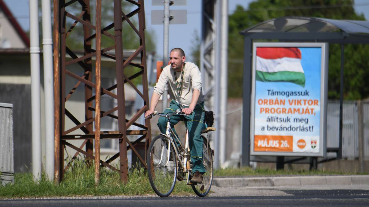Un ciclista pasea en la ciudad húngara de Csorna junto al cartel de la campaña del Gobierno para las elecciones europeas que dice: "Volvamos al programa de Orbán, paremos la inmigración".