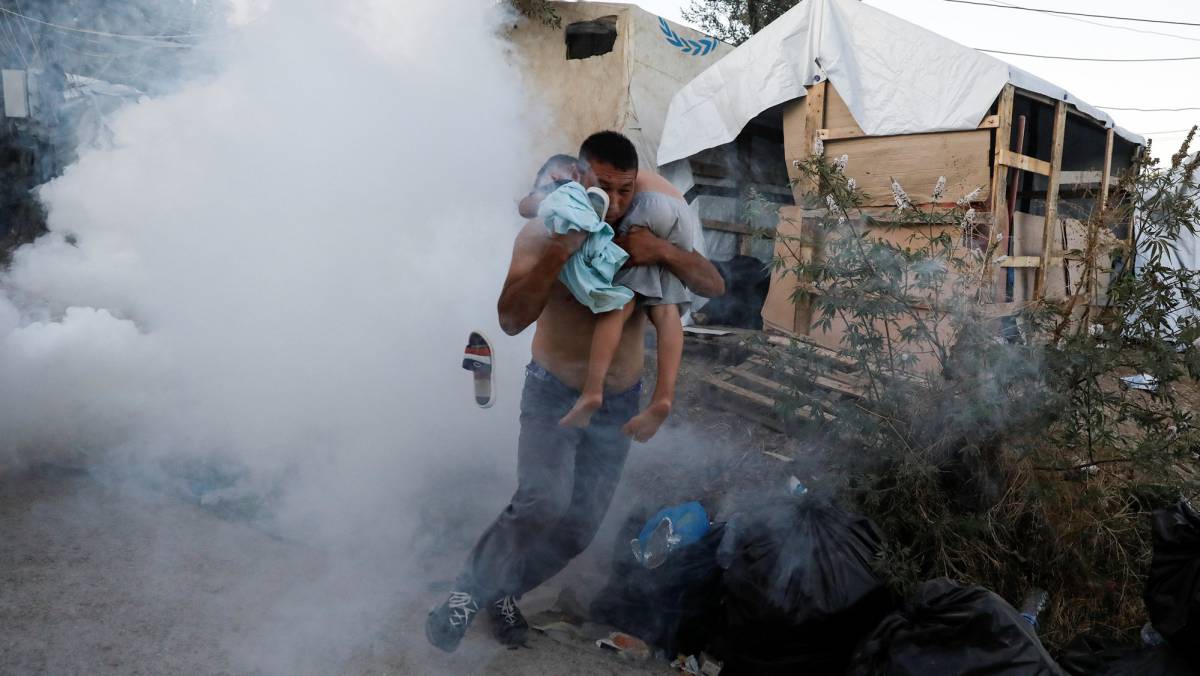 Un hombre escapa con un niño en brazos del gas lacrimógeno lanzado por los antidisturbios el domingo 29 de septiembre en el campo de refugiados de Moria, en la isla griega de Lesbos.