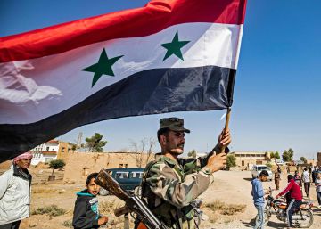 Un soldado del régimen ondea una bandera de Siria en la entrada occidental de Tal Tamr tras la entrada de las tropas regulares en esta localidad del norte de Siria.