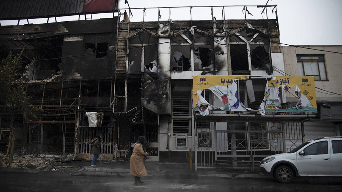 Dos viandantes, ante edificios quemados durante las protestas, en Teherán.
