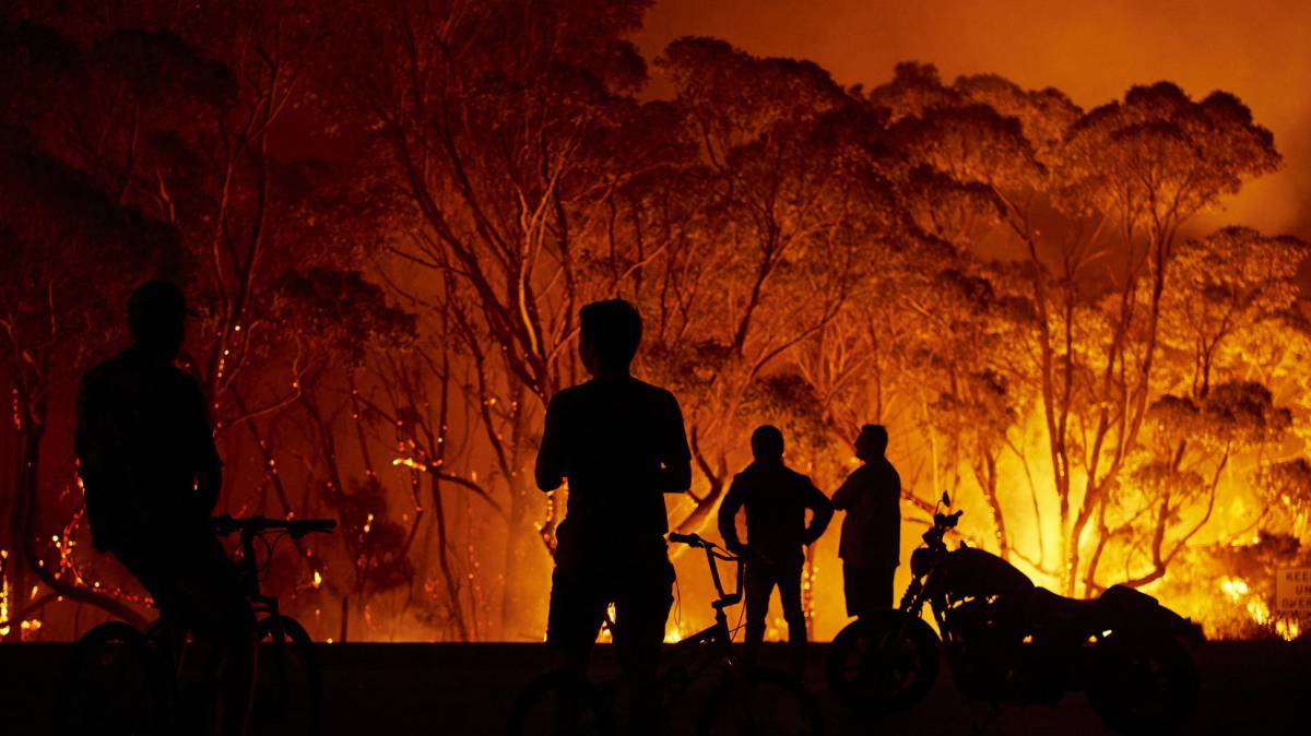 Unos vecinos observan las llamas en torno a su localidad, este sábado en Tabourie Lake (Nueva Gales del Sur).