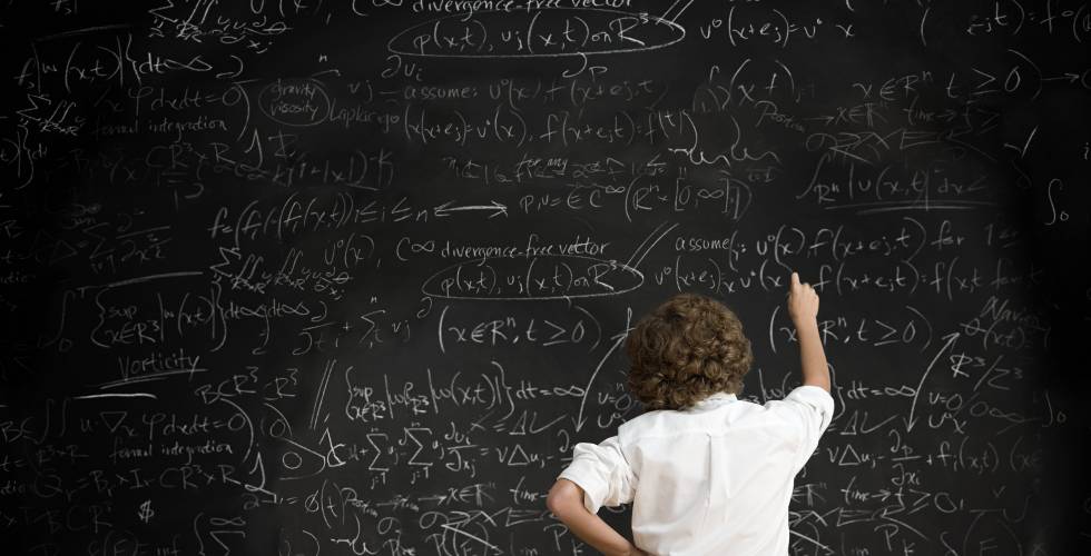 Un chico escribe en una pizarra llena de fórmulas.