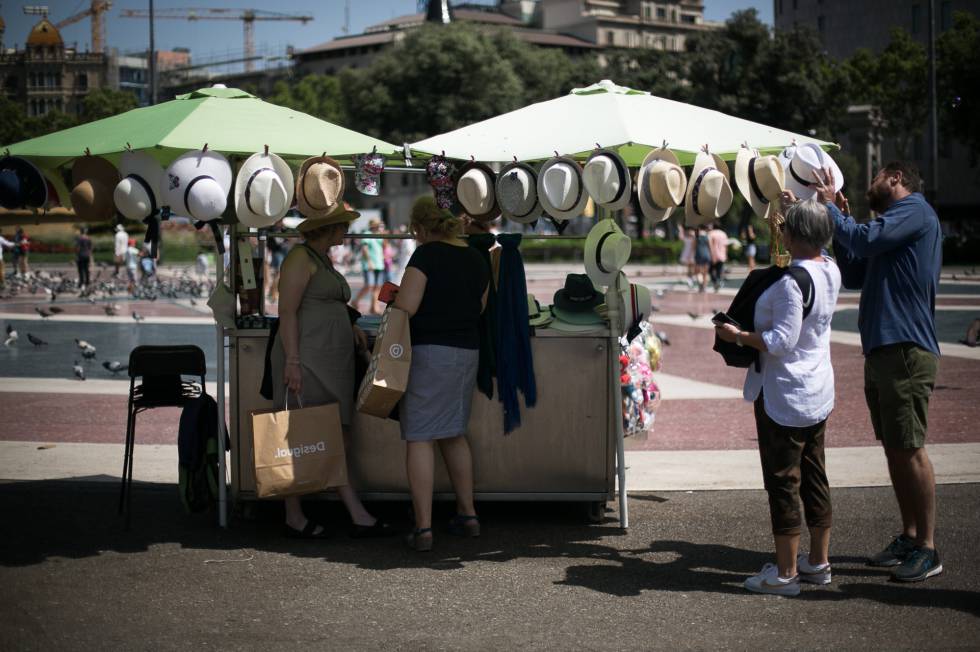 Varias personas compran sombreros para protegerse de la calor en plaza Catalunya de Barcelona.