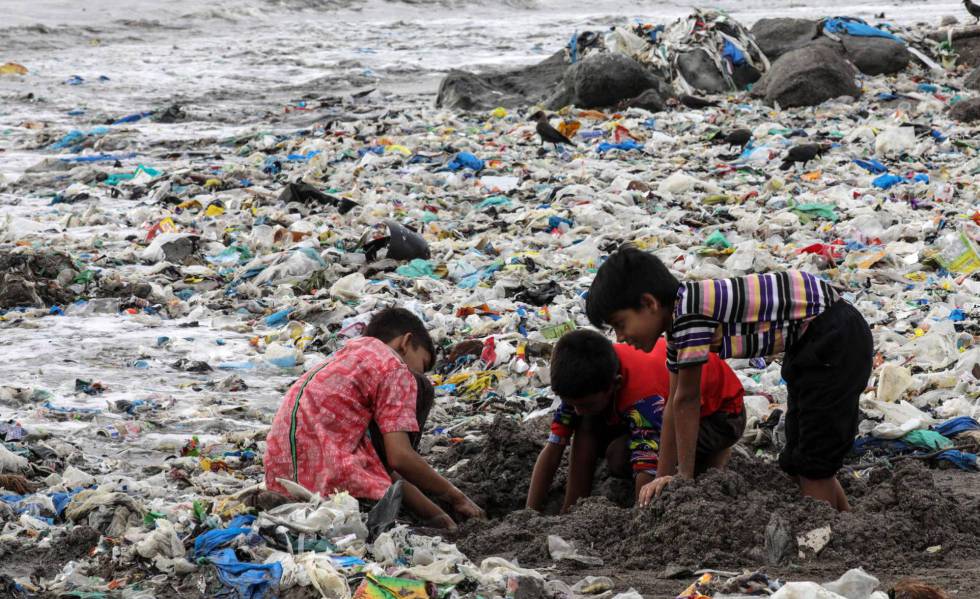 Varios niños juegan entre desechos de comida y plástico cerca de la costa del mar Arábigo, en la playa de Mahim, en Bombay (India)