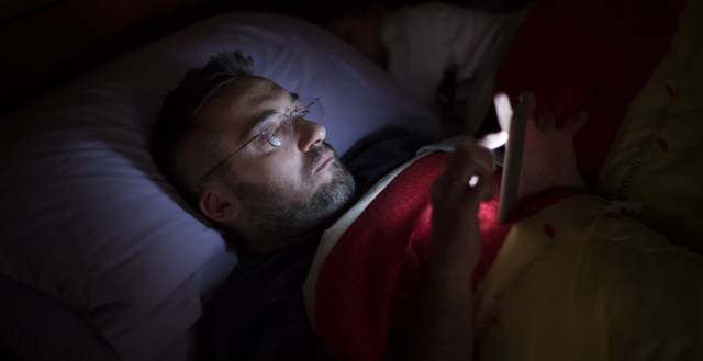 Un hombre lee a oscuras con su smartphone en la cama.