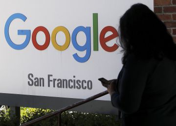Una persona consulta su móvil junto a un cartel de Google.