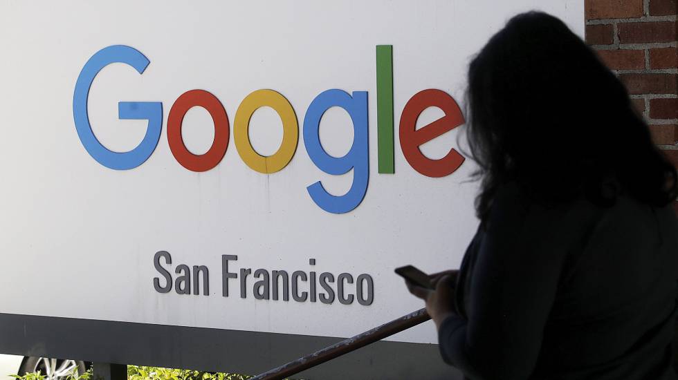 Una persona consulta su mÃ³vil junto a un cartel de Google.